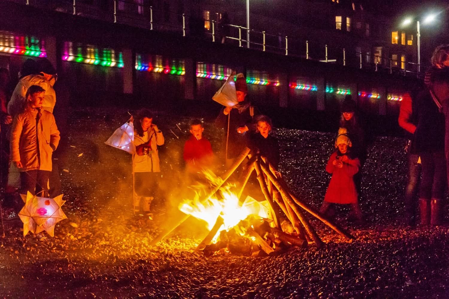 Families gathered around a beach bonfire with lanterns