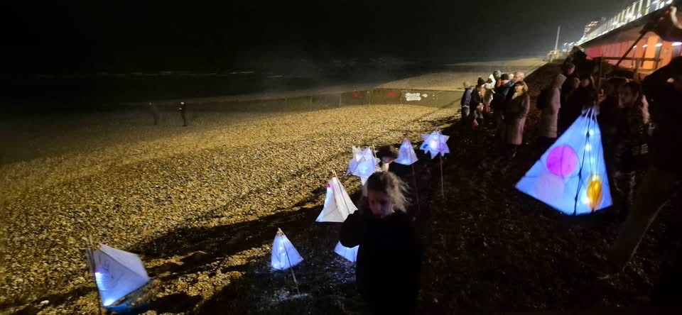 Children carrying lit lanterns along the beach