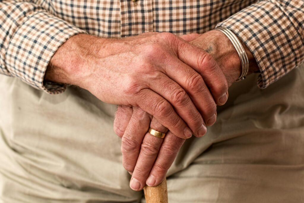 A close-up photograph of an old man resting his hands resting on his walking stick